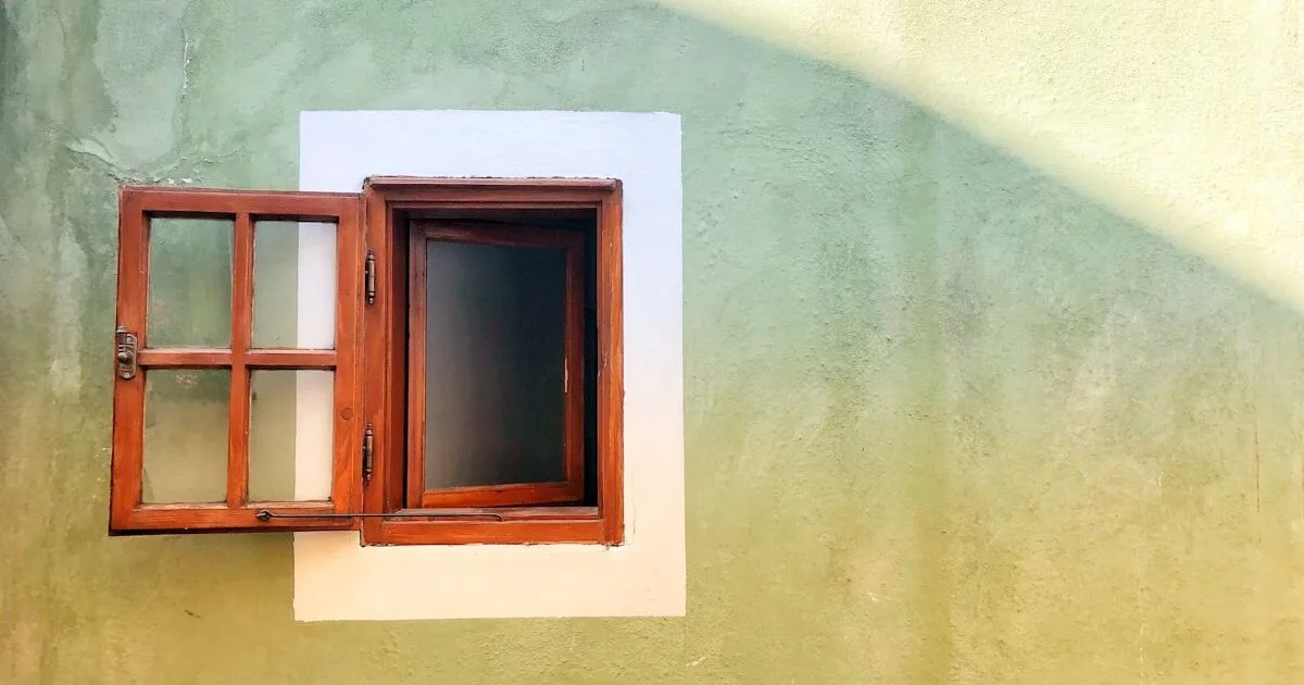 An open brown wooden window on a stucco wall